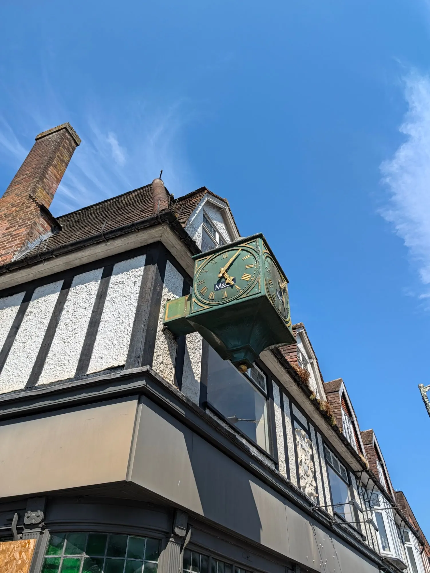The green and gold clock on the corner of 6 High Street, still showing the M&Co logo on its face, against a blue sky above the mock-Tudor frontage