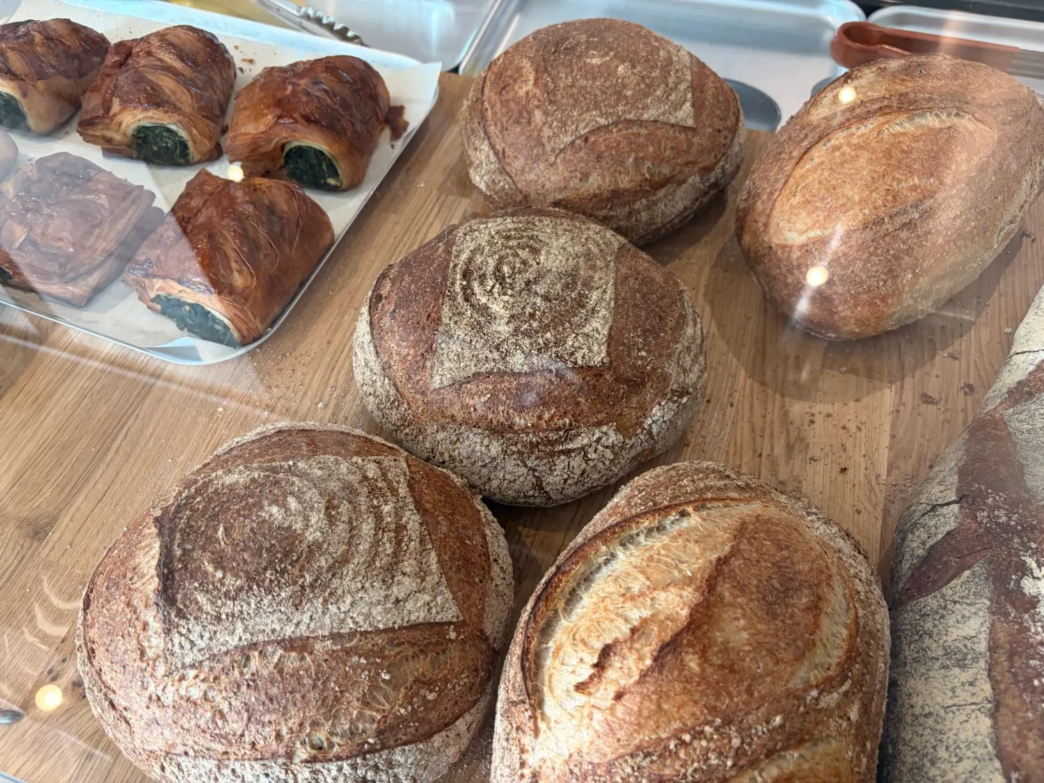 Round and oval sourdough loaves on a wooden counter beside a tray of green-filled pastries