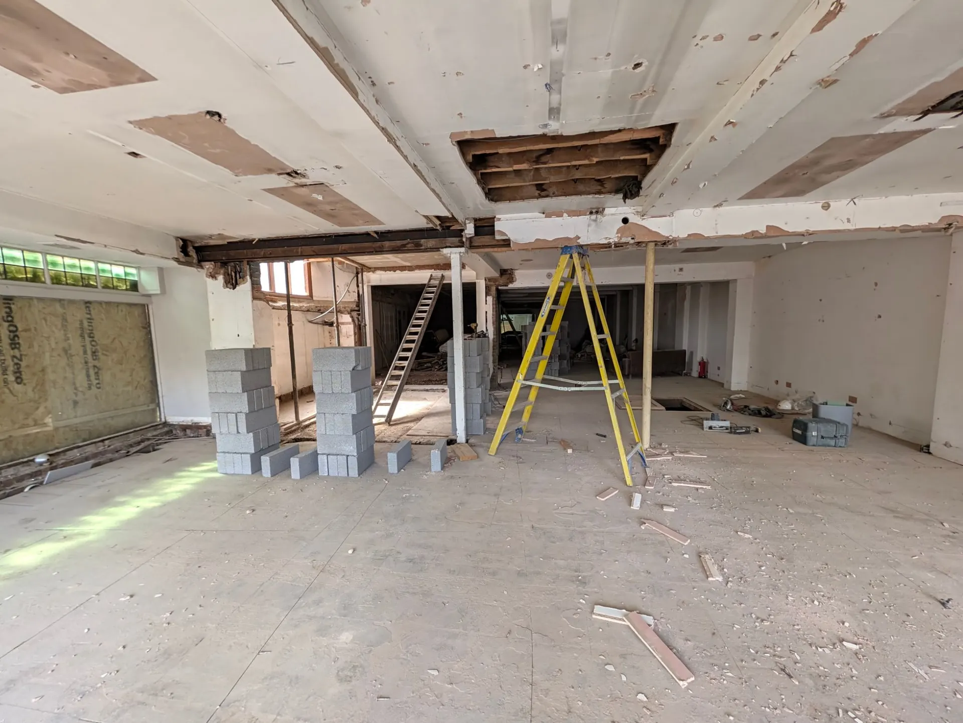The stripped-out ground floor of the former M&Co, with stacks of concrete blocks, a yellow stepladder, props supporting the ceiling and an opened-up section of ceiling joists